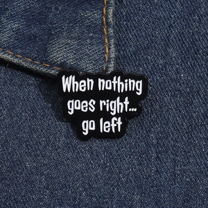 Close-up of black enamel cloud brooch with 'When nothing goes right go left' text on denim