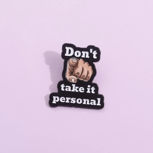 Enamel pin with finger pointing design and Don't take it personal text on purple backdrop