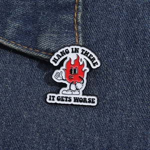 Détail d'un pin's émaillé flamme humoristique sur denim avec texte Hang In There