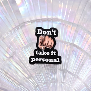 Gros plan d'un pin's en émail avec l'inscription « Don't take it personal » sur fond de verre