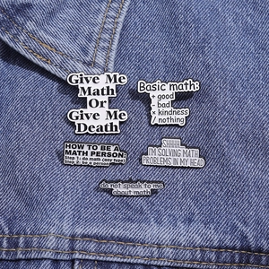 Detailed close-up of math-themed enamel pins on denim fabric showing text and symbols