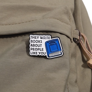 Detalle de pin esmaltado con cita de libro sobre bolso de lona verde oscuro