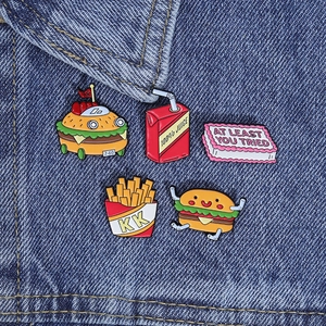 Detail of five enamel pins featuring burger and fries on blue denim background fabric