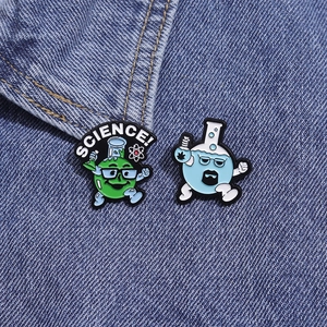 Detail view of science-themed enamel pins featuring cartoon beaker on blue denim fabric