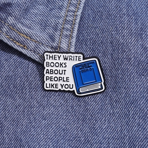 Detalle del pin esmaltado con frase y diseño de libro DSM-5 sobre tela vaquera azul