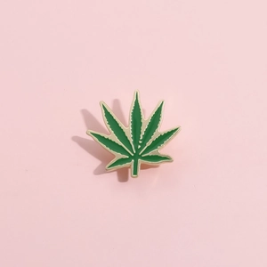 Green and gold enamel maple leaf brooch pin with vibrant metal plating on pink background
