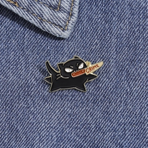 Détail macro du pin's chat noir émaillé avec couteau et texte CRIME sur du denim