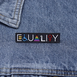 Detail view of the Equality enamel pin with rainbow symbols on a blue denim jacket