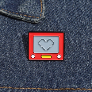 Macro detail of red vintage TV game console enamel pin with black heart icon on denim