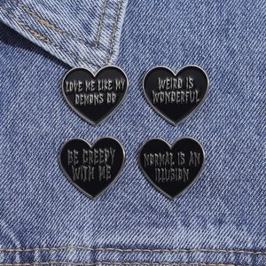 Close-up of four black heart enamel pins with gothic text on blue denim fabric