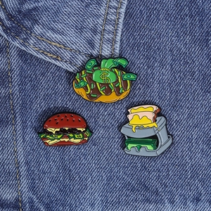 Detailed view of creative dollar-themed enamel pins on denim, including burger and donut pins