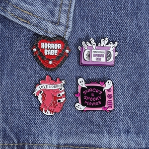 Detailed macro view of four horror-themed enamel pins pinned on a blue denim jacket