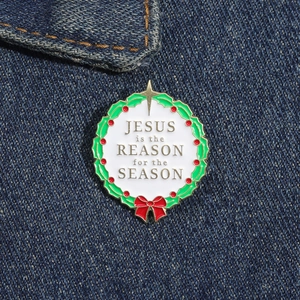 Detail of Christmas holly wreath enamel pin on denim showing Jesus is the Reason text