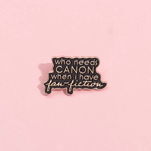 Detail of black enamel pin with golden border and creative text on pink background