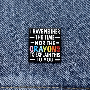 Square black enamel brooch with colorful CRAYONS lettering on blue denim fabric background