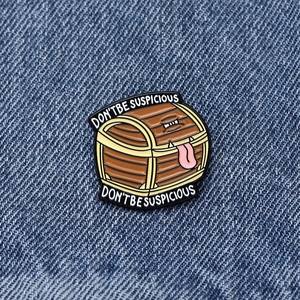 Close-up of Mimic Chest enamel pin with Don't Be Suspicious text on denim background