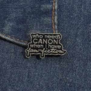 Macro shot of black enamel metal pin with fan-fiction quote on blue denim jacket