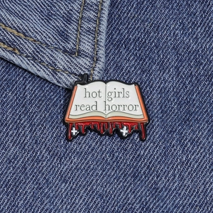 Close-up of Hot Girls Read Horror book enamel pin on a blue denim jacket background