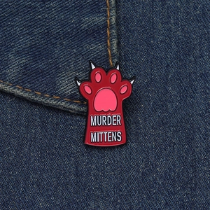 Close-up of a red cat paw enamel pin with Murder Mittens text on blue denim fabric
