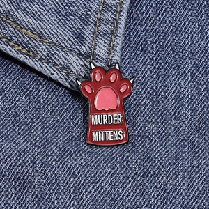 Creative Murder Mittens cat paw enamel pin featured on blue denim fabric background
