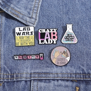 Close-up of 5 scientific enamel pins including Lab Wars and Steminist motifs on denim fabric
