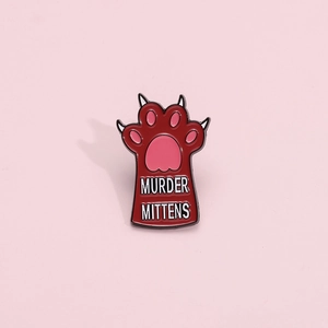 Detail of enamel cat paw pin with Murder Mittens slogan on light pink background