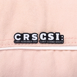 Detailed macro of enamel CRS and CSI letter brooches with humorous quotes on denim fabric