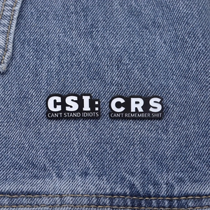 Macro shot of two funny black enamel pins with sarcastic text on dark denim fabric
