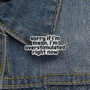 Schwarze Emaille-Anstecknadel Wolke mit Spruch auf Denim, Motiv Reizüberflutung