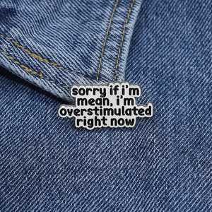 Detail-Emaillenadel mit 'sorry if i'm mean' Text auf blauem Denim-Jeansstoff