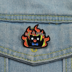Detail of Let It Burn black cat enamel pin with orange flames on denim jacket