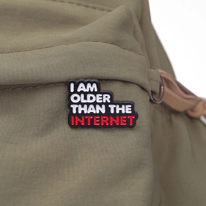 Macro detail of enamel pin with 'I AM OLDER THAN THE INTERNET' text on green fabric
