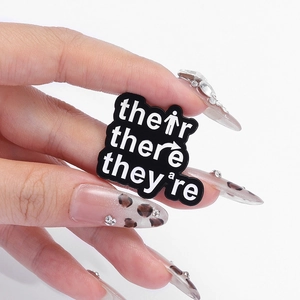 Close-up of funny English grammar enamel pin held by hand with leopard print nails