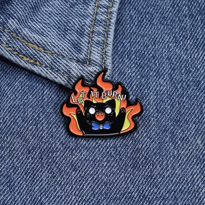 Detail of Let It Burn black cat enamel pin pinned onto a blue denim jacket fabric