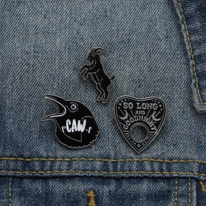 Detailed view of three black enamel pins featuring a goat, crow, and heart on denim