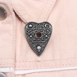 Detailed close-up of a Gothic heart Ouija board enamel pin on a pink denim jacket