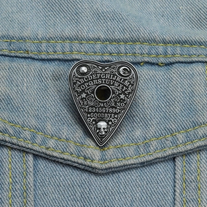 Gothic heart Ouija board enamel pin with skull detail on blue denim jacket pocket