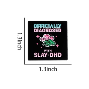 Detail view of square black enamel frog pin with Slay-DHD text measuring 1.3 by 1.3 inches