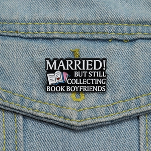 Détail d'un pin's émaillé noir sur veste en jean avec slogan de livre et motif de cœur