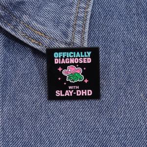 Detail of square frog brooch with pink cowboy hat on denim fabric background