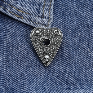 Detail of gothic Ouija heart enamel pin with letters and skull on denim background