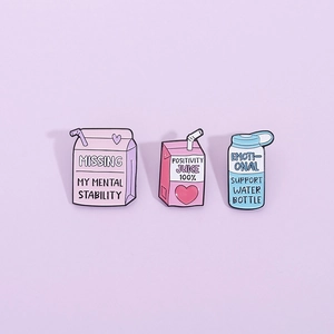 Cute enamel pins featuring cartoon milk box and juice bottle designs on a purple background