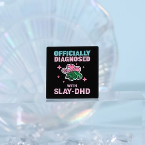 Detail of square enamel pin featuring a green frog in a pink cowboy hat with star motifs