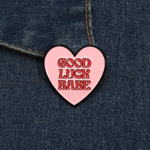Detail of pink heart enamel pin with Good Luck Babe text on blue denim fabric