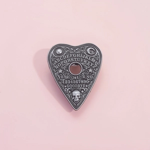 Gothic Ouija planchette metal brooch with alphabet and skull details on pink background