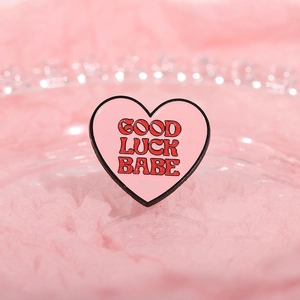 Detail der rosa Emaille-Anstecknadel mit Good Luck Babe Text auf Stoffhintergrund
