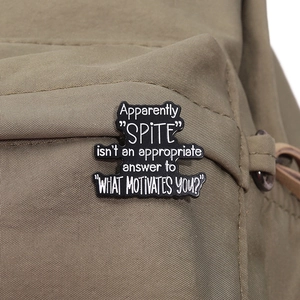 Close-up of black enamel pin with white quote on a beige canvas bag fabric