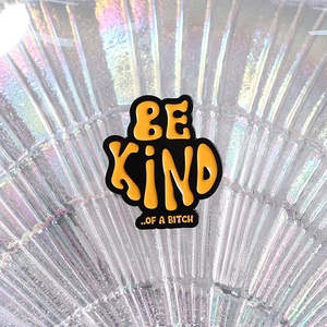 Gros plan sur le pin's émaillé jaune et noir avec texte BE KIND OF A BITCH gras