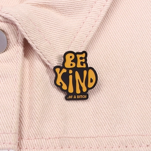 Detail of metal enamel pin with BE KIND OF A BITCH text on pink denim fabric