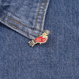 Broche artistique en métal avec main tenant rose blanche et texte Bad Seed sur denim